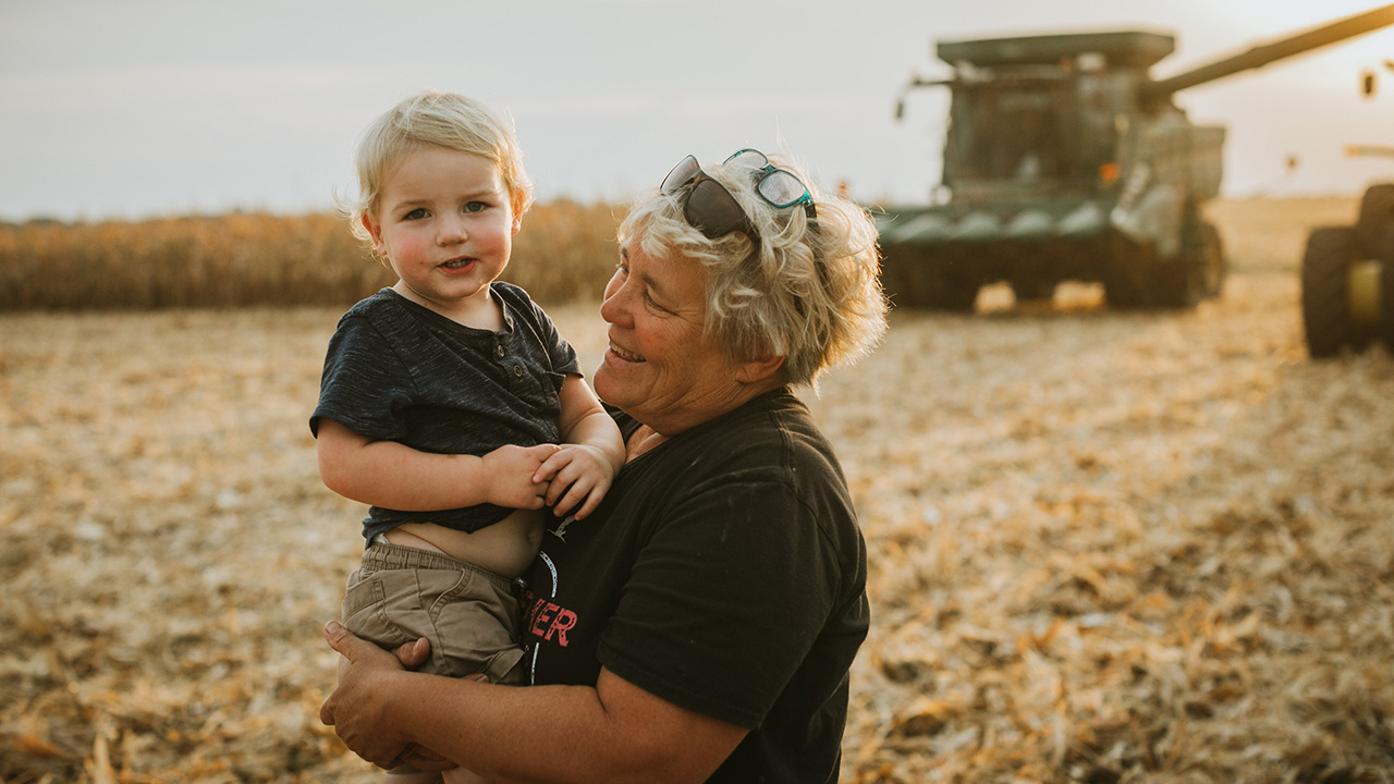 Grandma holding grandson in field.