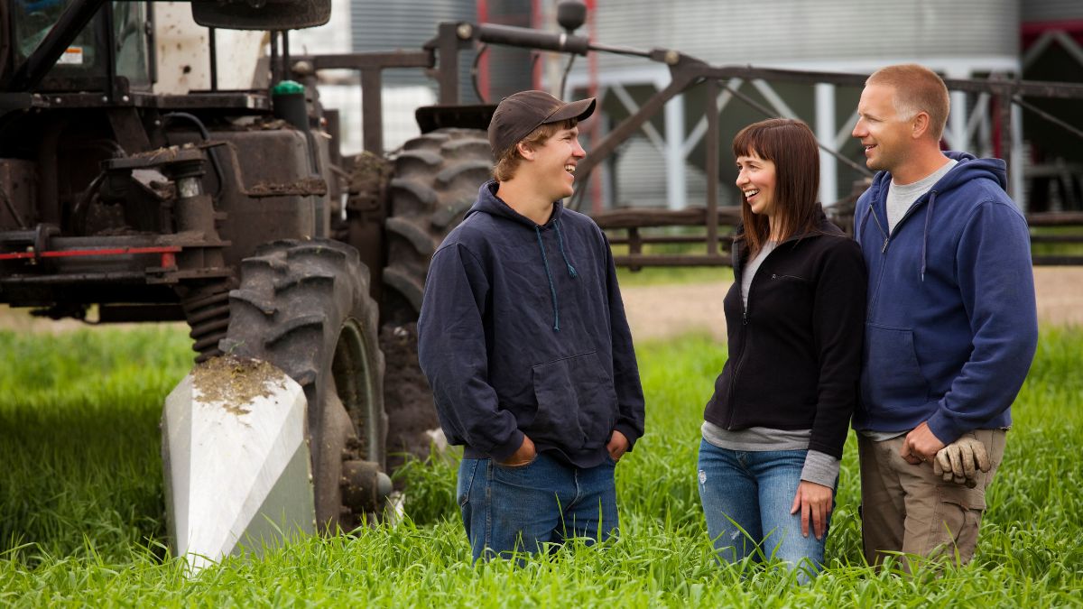 parents and son on farm in front of machinery, smiling.