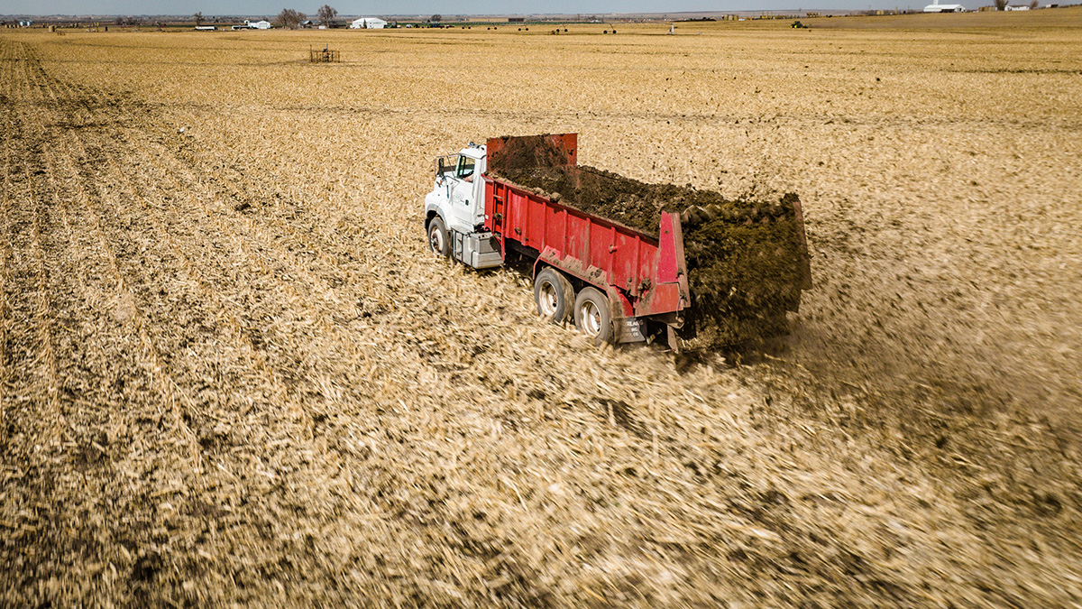 Truck spreading manure on field.