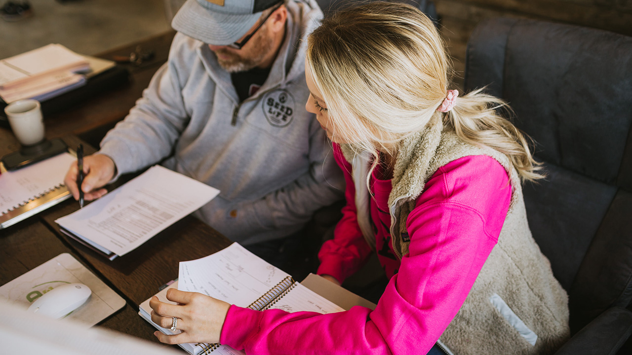 Two people reviewing documents at a wooden desk in a casual setting.