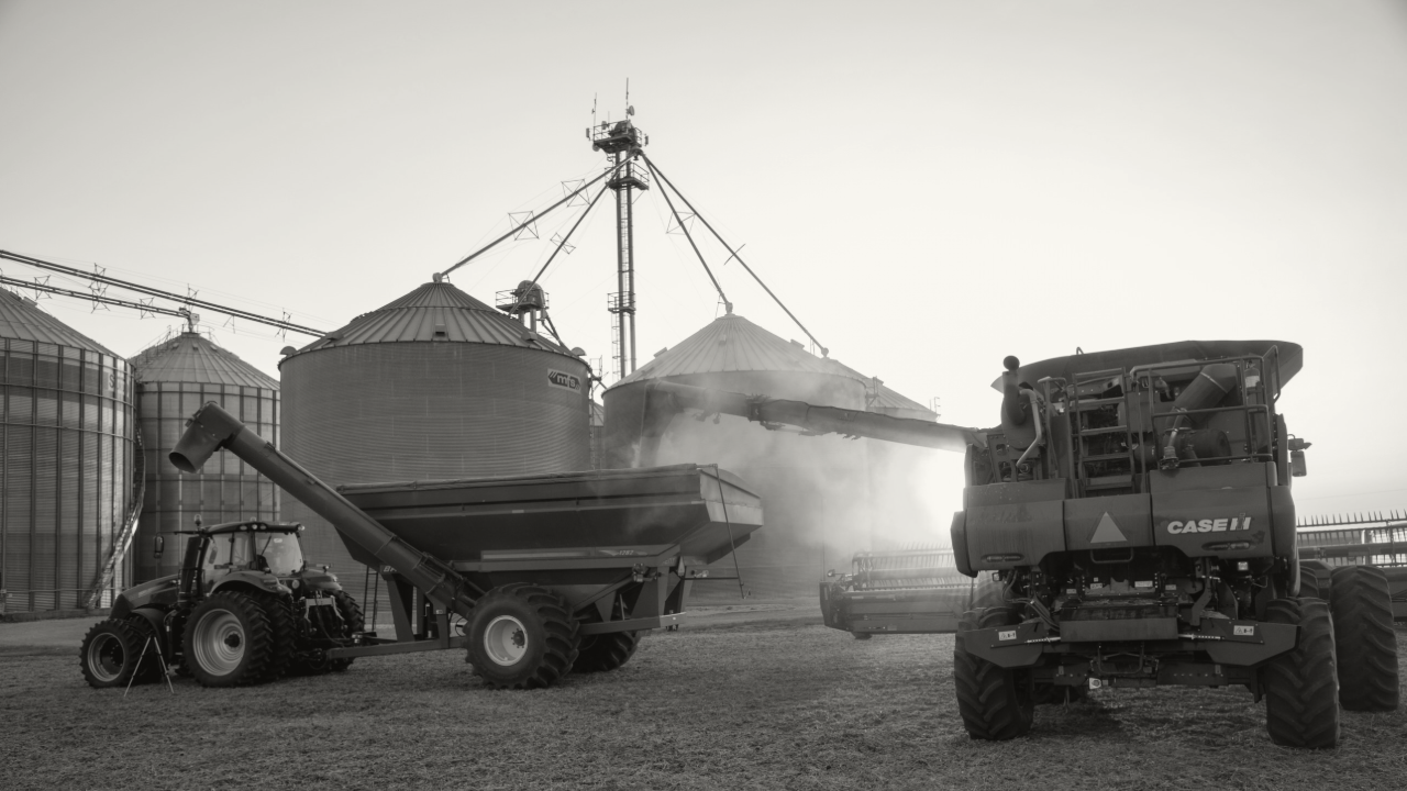 Photo of a grain bin in the background of a grain cart, tractor, and semi truck.