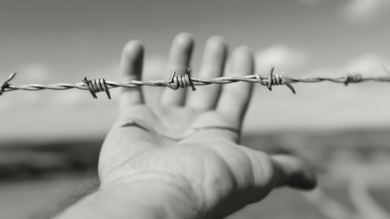 Photo of a hand under a barded-wire fence.