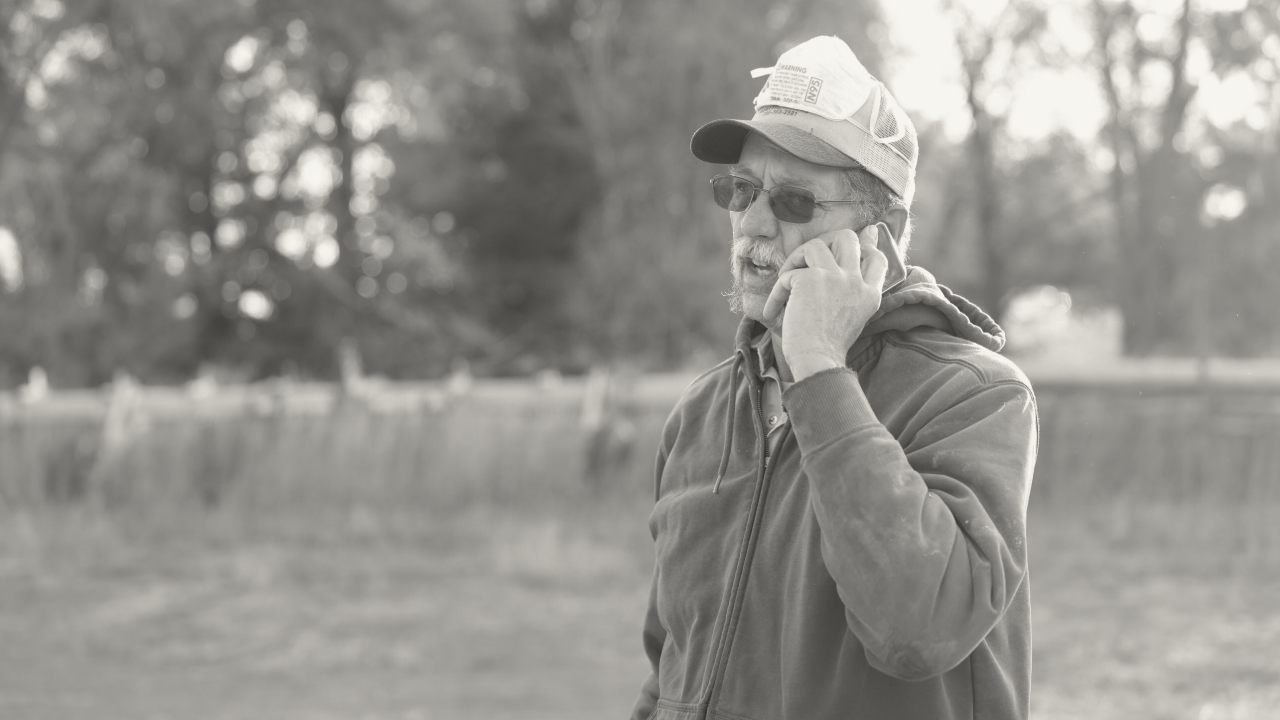 A farmer talks on a cell phone in the lawn in front of a corn field.