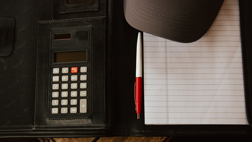 Calculator, pen, notebook, and cap on a dark desk folder.