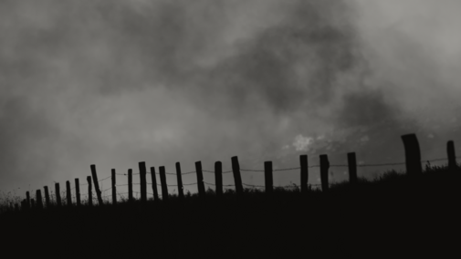 Photo of a fire burning behind a fenceline.