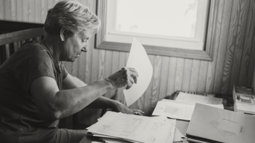 Person sitting at a table sorting papers near a window in a wooden-paneled room.