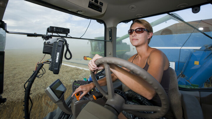 Photo of a woman driving a tractor inside the cab.