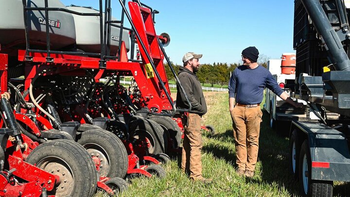 Two men talking between farm machinery.