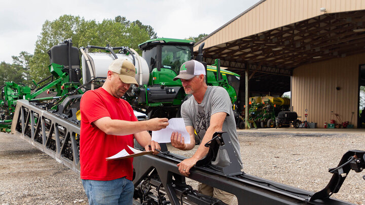 Photo of two farmers sharing paperwork at a sprayer.