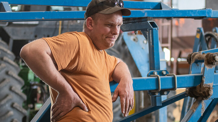 Photo of a farmer leaning on machinery in a shed.