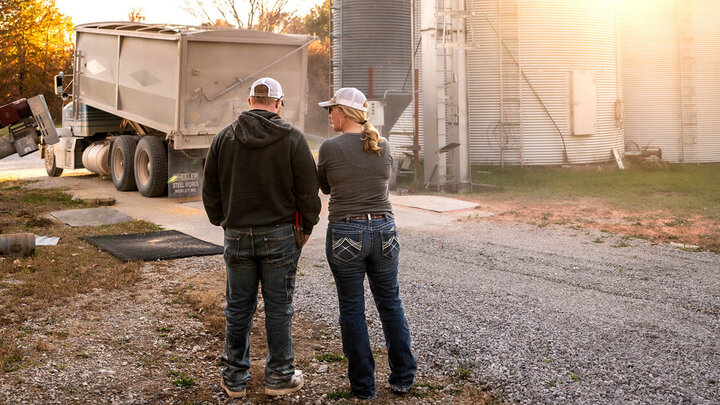 Photo of a male and female farmer standing near a semi about to unload grain.