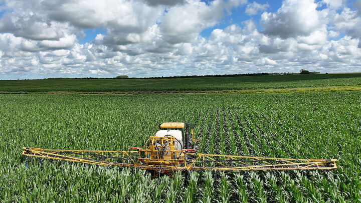 Y dropping corn in a field on a bright day with many clouds in the sky.