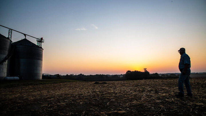 Man near grain bins at dusk.