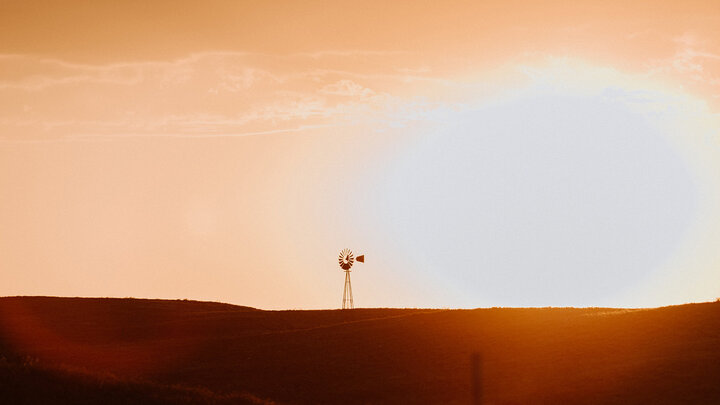 Photo of a windmill on a hill at sunset.