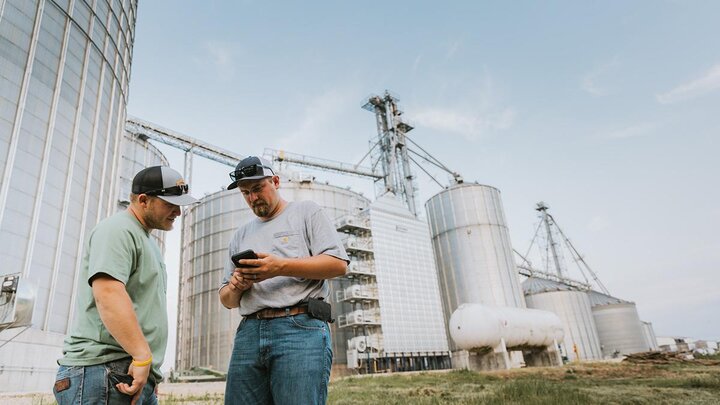 Farmers talking in front of grain bins.