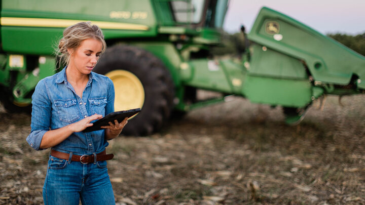 Photo of a woman outside a combine with a tablet.