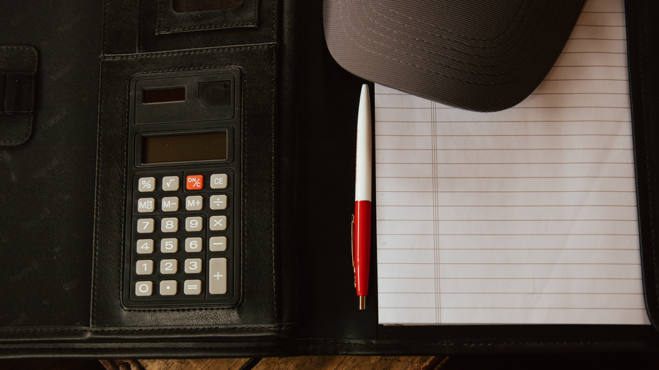 Calculator, pen, notebook, and cap on a dark desk folder.