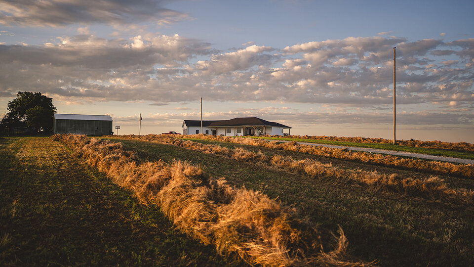 Photo of a farm house amid a field with cut hay.
