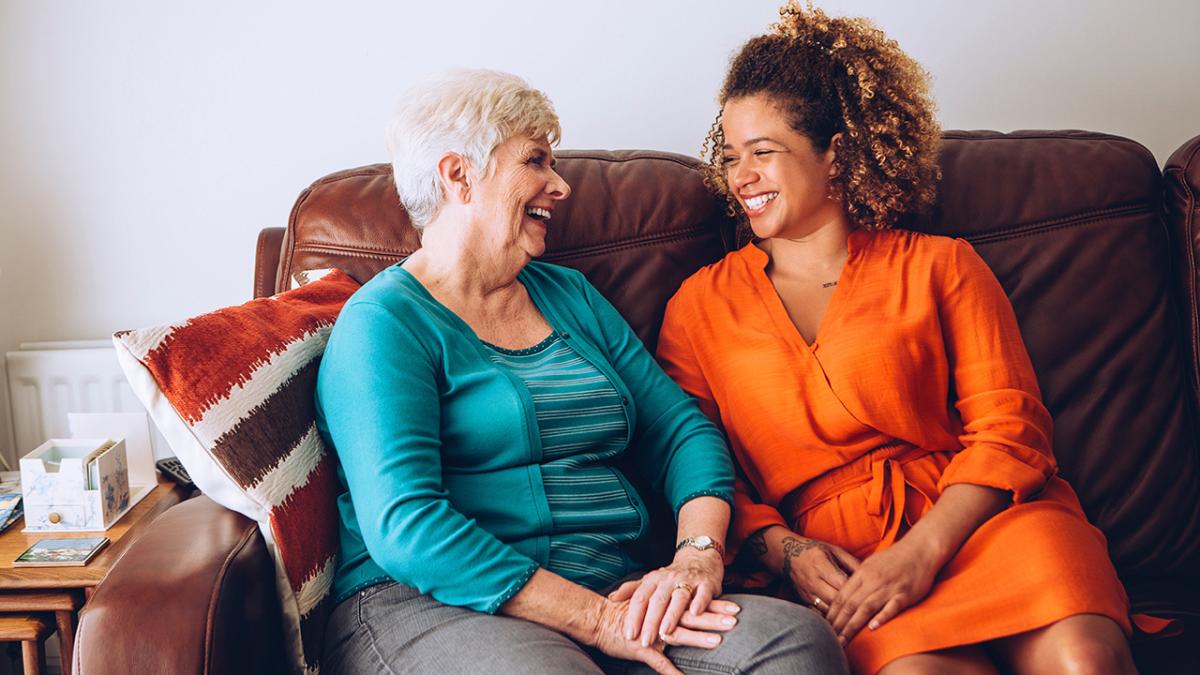 Two generations of women sitting next to each other, laughing on the couch.