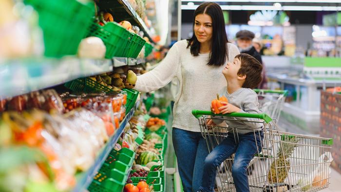 Woman shopping in produce section of grocery store with young child in the cart.