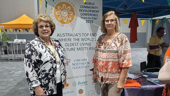 Cheryl Burkhart-Kriesel and Marilyn Schlake posing in front of a conference banner at the World Community Development Conference.